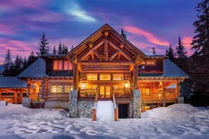 A log cabin with a prominent entrance, stone foundation, and a balcony overlooking a snowy landscape. - Mountain 4BR with hot tub, game room & fireplaces (Snoqualmie Pass)