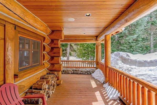 A wooden log cabin with a covered porch, stone wall, and a view of a snowy landscape. - Mountain 4BR with hot tub, game room & fireplaces (Snoqualmie Pass)