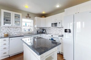 Une cuisine avec des meubles blancs, un plan de travail en granit, un four encastré et un four à micro-ondes.