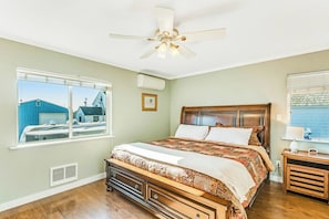 Ein Schlafzimmer mit einem großen Bett, einem Deckenventilator und einem Fenster mit Blick auf Gebäude.