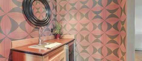 A bathroom with a patterned wallpaper, a sink with a mirror, and a potted plant.