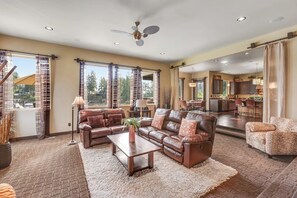 A spacious living room with a brown leather sofa, a coffee table, and a view of the kitchen and dining area through large windows. - 5BR luxury lake home with private beach & dock (Fox Island)