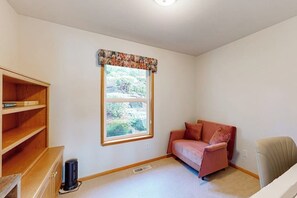 Une pièce avec une fenêtre, un canapé, un fauteuil et une bibliothèque.