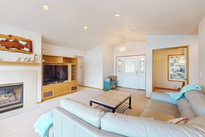 A living room with a fireplace, a large TV, a sofa, and a dining area. - 3 BR Waterfront home with beach access (Shelton)