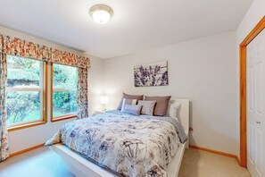 A bedroom with a bed, two windows with curtains, a bedside table with a lamp, and a door. - 3 BR Waterfront home with beach access (Shelton)
