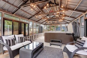 Ein überdachter Außenbereich mit einer Couch, einem Tisch und einer Whirlwanne.
