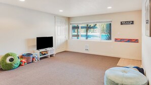 Sala de estar com televisão, brinquedos e janela com vista para uma piscina.