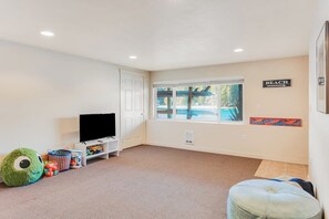 A living room with a television, toys, and a window with a view of a pool. - Amazing 3BR Bayview Dog Friendly - Balcony (Allyn)