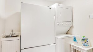 Cozinha compacta com geladeira, micro-ondas, pia e uma pequena mesa com produtos de limpeza.