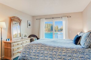 Ein Schlafzimmer mit einem großen Bett, einem Schminktisch, einem Spiegel und einem Fenster mit Meerblick.