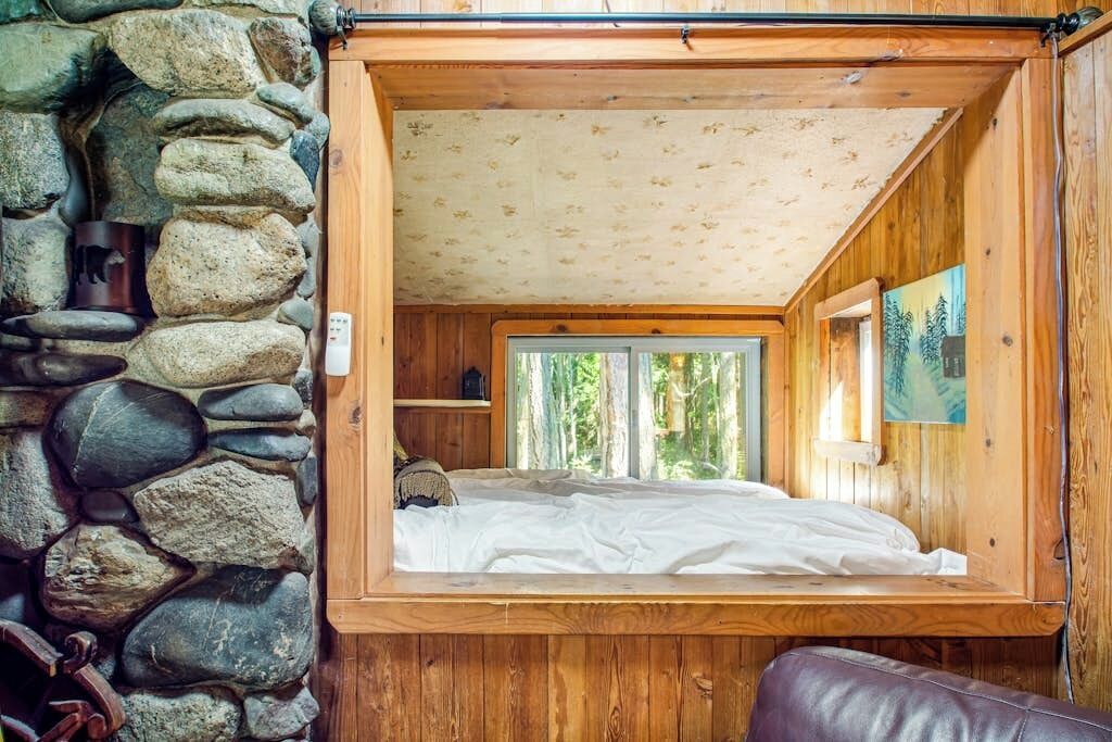 Un dormitorio con pared de piedra, techo de madera y una ventana.