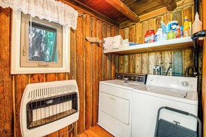 Ett tvättrum med torktumlare, tvättmaskin och ett fönster med en spetsgardin.