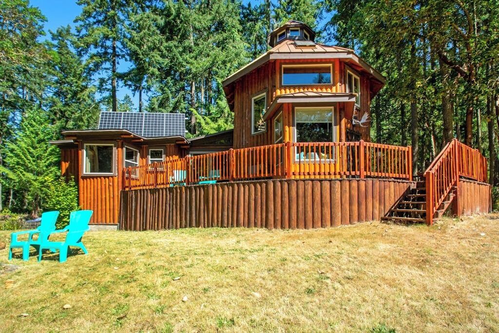 A wooden cabin with a deck, surrounded by trees.