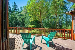 A wooden deck with two chairs and a railing, surrounded by trees.