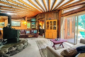 A rustic cabin interior with a stone fireplace, wooden walls, a leather sofa, and a sliding glass door to the outdoors.