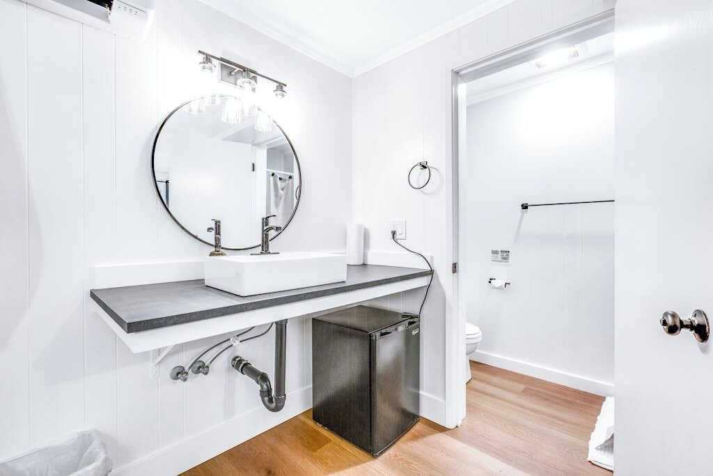 Un baño moderno con tocador blanco, un espejo redondo, inodoro y zona de ducha.