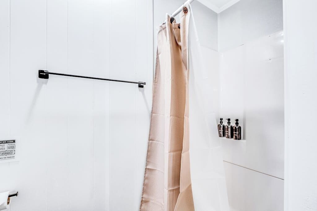 A bathroom with a white shower curtain, a towel rack, and a wall-mounted soap dispenser.