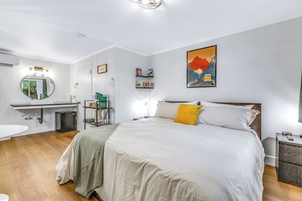 Une chambre d’hôtel comprenant un lit, une table de chevet, une commode, un miroir, un lavabo et une fenêtre.