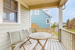 Eine Veranda mit einem runden Holztisch und zwei Stühlen, ein Fenster und Blick auf ein blaues Haus.