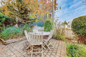 Eine Terrasse mit einem runden Tisch und Stühlen, umgeben von Pflanzen und einem weißen Zaun.