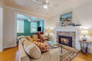 A living room with a fireplace, a sofa, a television, and a ceiling fan. - 4BR Seabrook property - carriage house & yard (Pacific Beach)