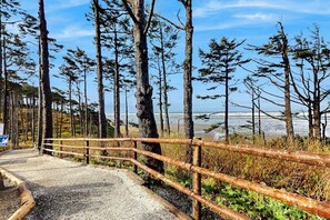 A gravel path with a wooden fence leading to a beach with tall trees. - 4BR Seabrook property - carriage house & yard (Pacific Beach)