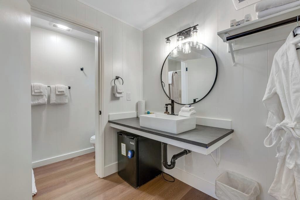 A modern bathroom with a white sink, a round mirror, and a towel rack.