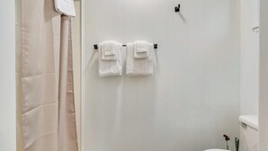 A bathroom with a toilet, a towel rack with two towels, and a shower curtain.