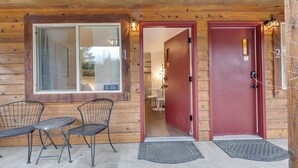 A wooden cabin with a red door, a window, and two metal chairs outside.