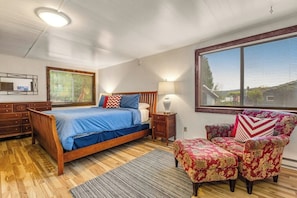 Une chambre à coucher avec un lit, une chaise, une table de chevet, une lampe et une fenêtre.