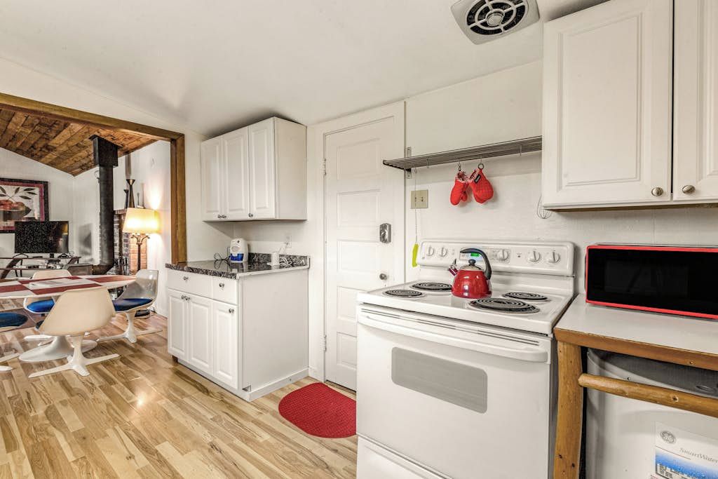 A kitchen with white cabinets, a red kettle, and a microwave.