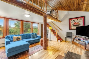 Un salon spacieux avec un canapé d’angle bleu, un escalier en bois et un grand téléviseur.