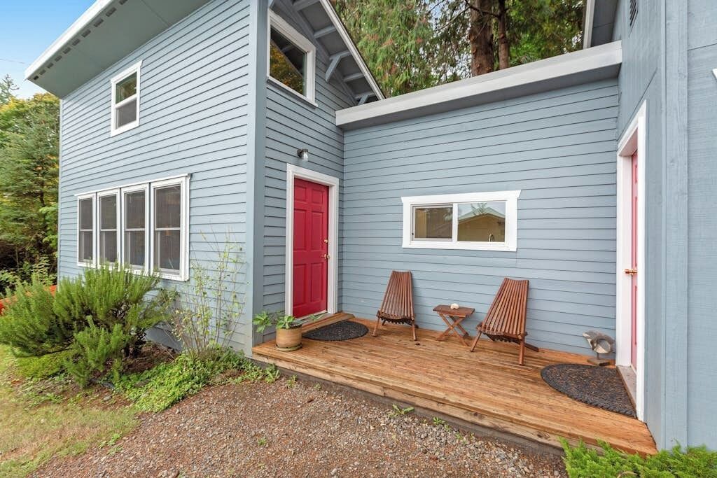 Ein zweistöckiges Haus mit einer Holzterrasse, einer roten Tür und zwei Stühlen.