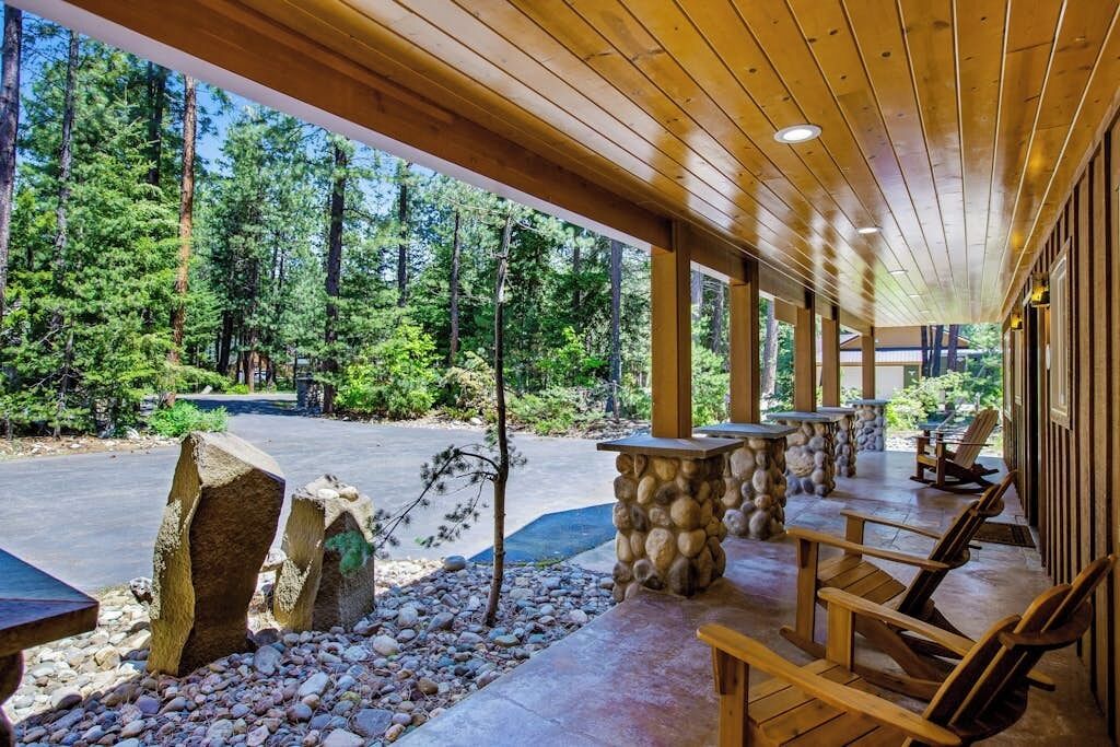 Ein überdachter Außenbereich mit Holzbänken und Steinsäulen, umgeben von einem Wald.