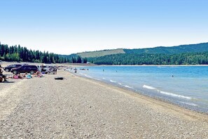 A pebbled beach with vehicles and people, a clear sky, and forested hills in the background. - Spacious 5BR - Chef's Kitchen- Fireplace (Ronald)