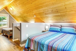 A bedroom with a sloped ceiling, a bed with striped bedding, a nightstand, and a window. - Dog-friendly, mountainview 1BR- walk to skiing (Snoqualmie Pass)