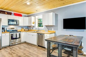 A modern kitchen with white cabinets, stainless steel appliances, a wooden countertop, and a large flat-screen TV mounted on the wall. - Dog-friendly, mountainview 1BR- walk to skiing (Snoqualmie Pass)