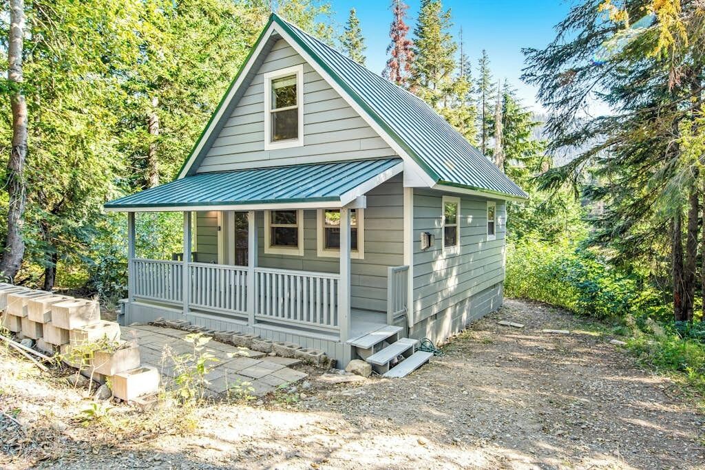 Une petite cabane dotée d’un porche, entourée d’arbres.