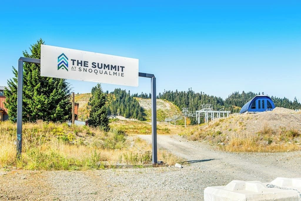 A sign for 'The Summit at Snoqualmie' with a clear sky and a dirt road leading to a blue tent-like structure.