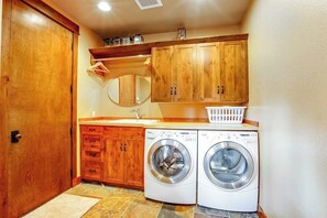 A laundry room with two front-loading washing machines, wooden cabinets, a mirror, and a laundry basket. - 3BR Suncadia Resort house with hot tub & fireplace (Cle Elum)