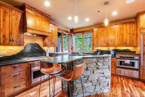 A kitchen with wooden cabinets, a stone island, and bar stools. - 3BR Suncadia Resort house with hot tub & fireplace (Cle Elum)