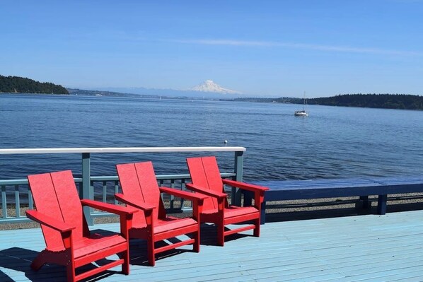 Une terrasse avec des chaises rouges donnant sur une étendue d’eau, avec une montagne visible au loin.