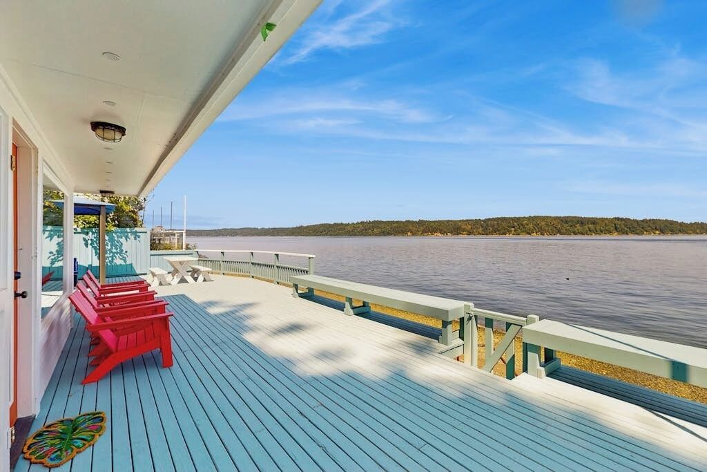 A wooden deck with benches, a railing, and a view of a calm body of water and distant land.