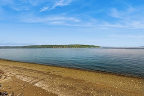 Un lac paisible, avec une rive de galets et une île boisée qui se dessine à l’horizon.