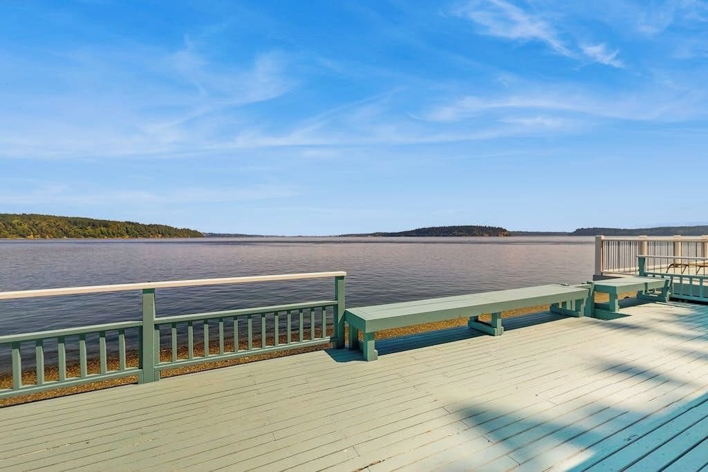 Un muelle de madera con bancos, barandilla y vista a un lago tranquilo.