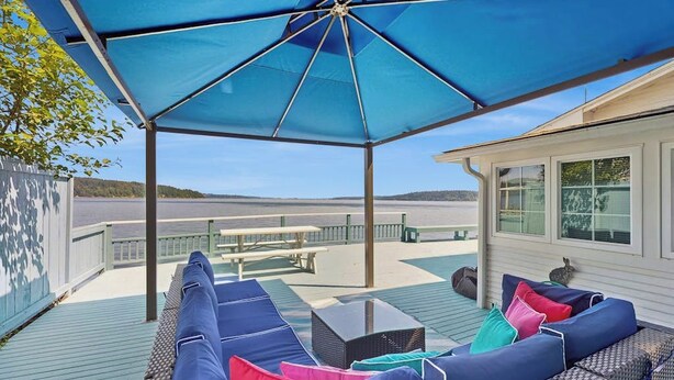 An outdoor deck with a covered seating area, a table, and a view of the water.