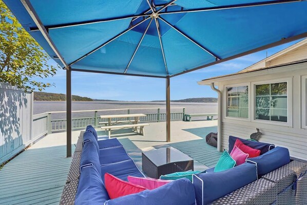 An outdoor deck with a covered seating area, a table, and a view of the water.