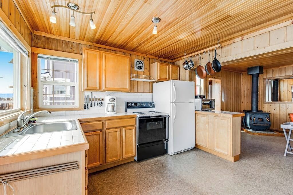 Cocina con armarios de madera, estufa, refrigerador y ollas colgantes.