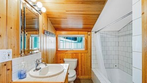 Een badkamer met houten lambrisering, een wastafel, toilet en bad.