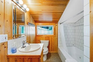Une salle de bain aux murs lambrissés, équipée d’un lavabo, de toilettes et d’une baignoire.